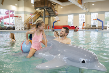 Father and daughter playing in indoor pool at Hershey Lodge, daughter floating ontop of fun dolphin floaty.