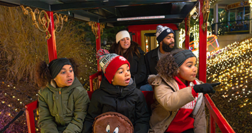 Family with three small children riding the Christmas train together and looking at lights .